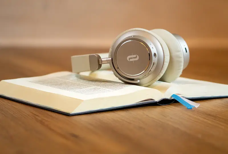 A pair of silver headphones rests on an open book, with a wooden background creating a cozy study atmosphere.